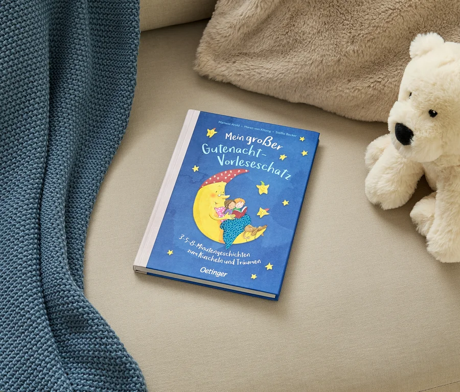 Ein blaues Kinderbuch „Mein großer Gutenacht-Vorleseschatz“ mit Mond-Illustration, eine blaue Decke und ein weißer Teddybär auf einem beigen Sofa.