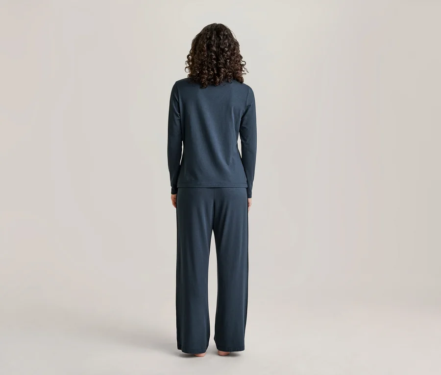 Eine Person mit lockigem dunklem Haar steht mit dem Rücken zur Kamera und trägt ein dunkelblaues Langarmshirt und passende weite Hosen.