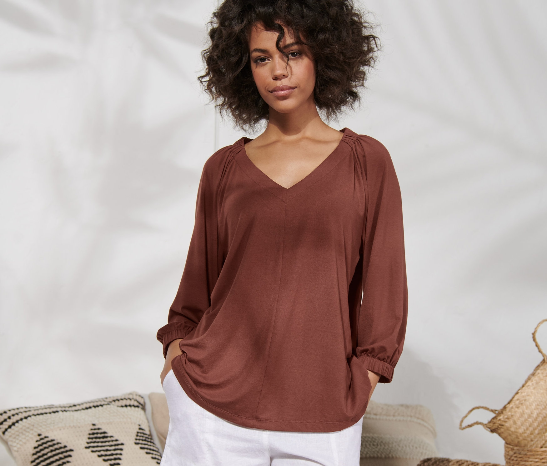 Frau posiert in terrakottafarbenem Shirt mit Raffung und weißen Shorts.