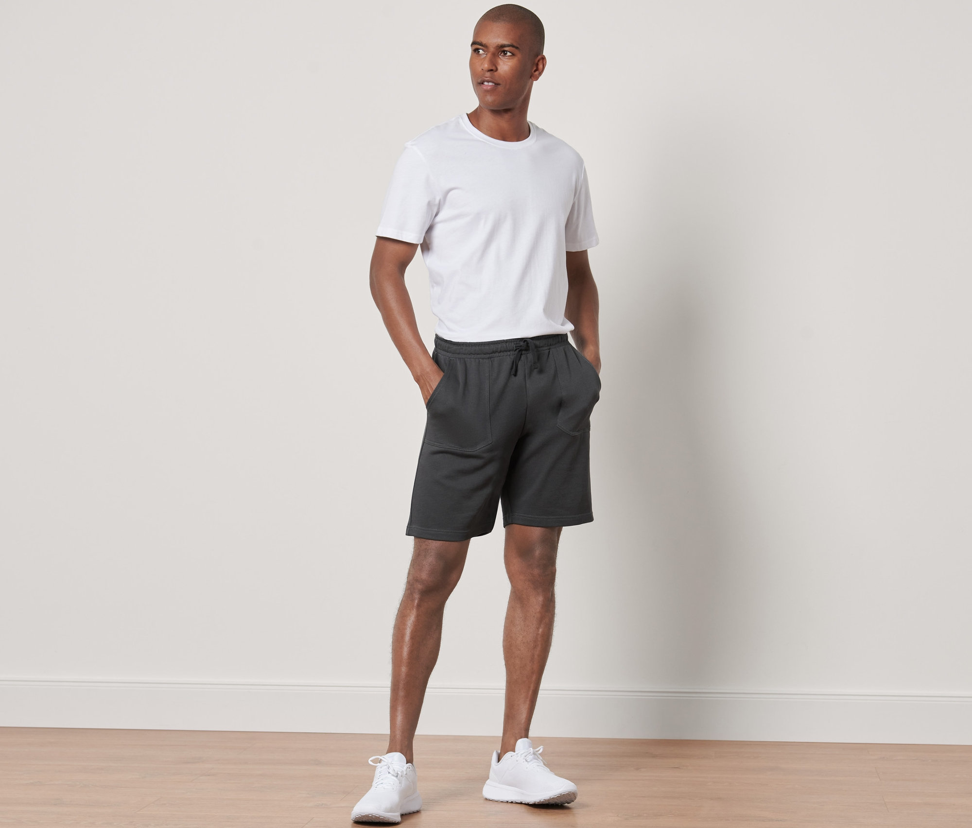 Mann steht mit Händen in den Taschen der Sweatshorts.