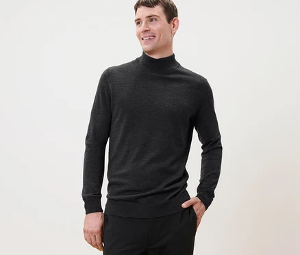 Mann mit kurzen Haaren posiert in einem anthrazitfarbenen Merino-Pullover und einer schwarzen Hose.