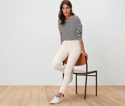 Frau sitzt auf einem Stuhl und trägt cremeweiße Colored Jeans ‒ Fit »Emma« und ein gestreiftes Shirt.