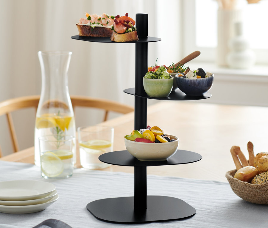 Schwarze Etagere mit drei Ebenen mit Speisen auf einem Holztisch.