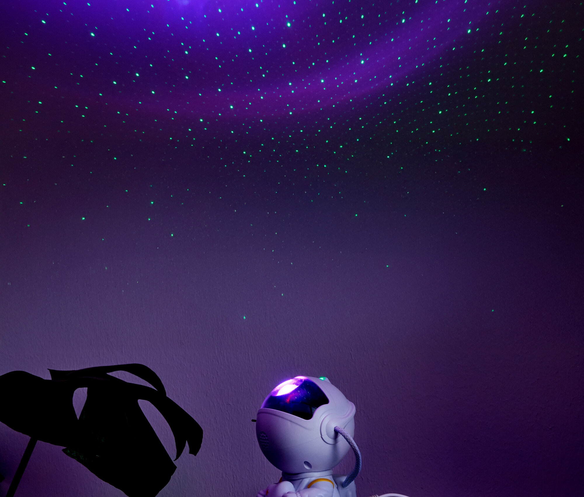 Astronaut sitzt auf einem Regal unter einer Projektion des Sternenhimmels.