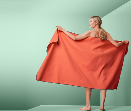 Frau hält XL-Outdoor-Badetuch, orange, ca. 100 x 200 cm.