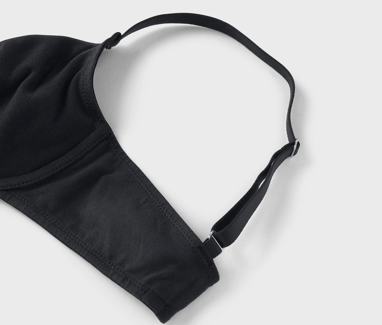 Detailaufnahme eines schwarzen BHs mit verstellbaren Trägern auf grauem Hintergrund.
