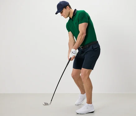 Mann mit grünem Poloshirt und Funktionsshorts beim Golfspielen.