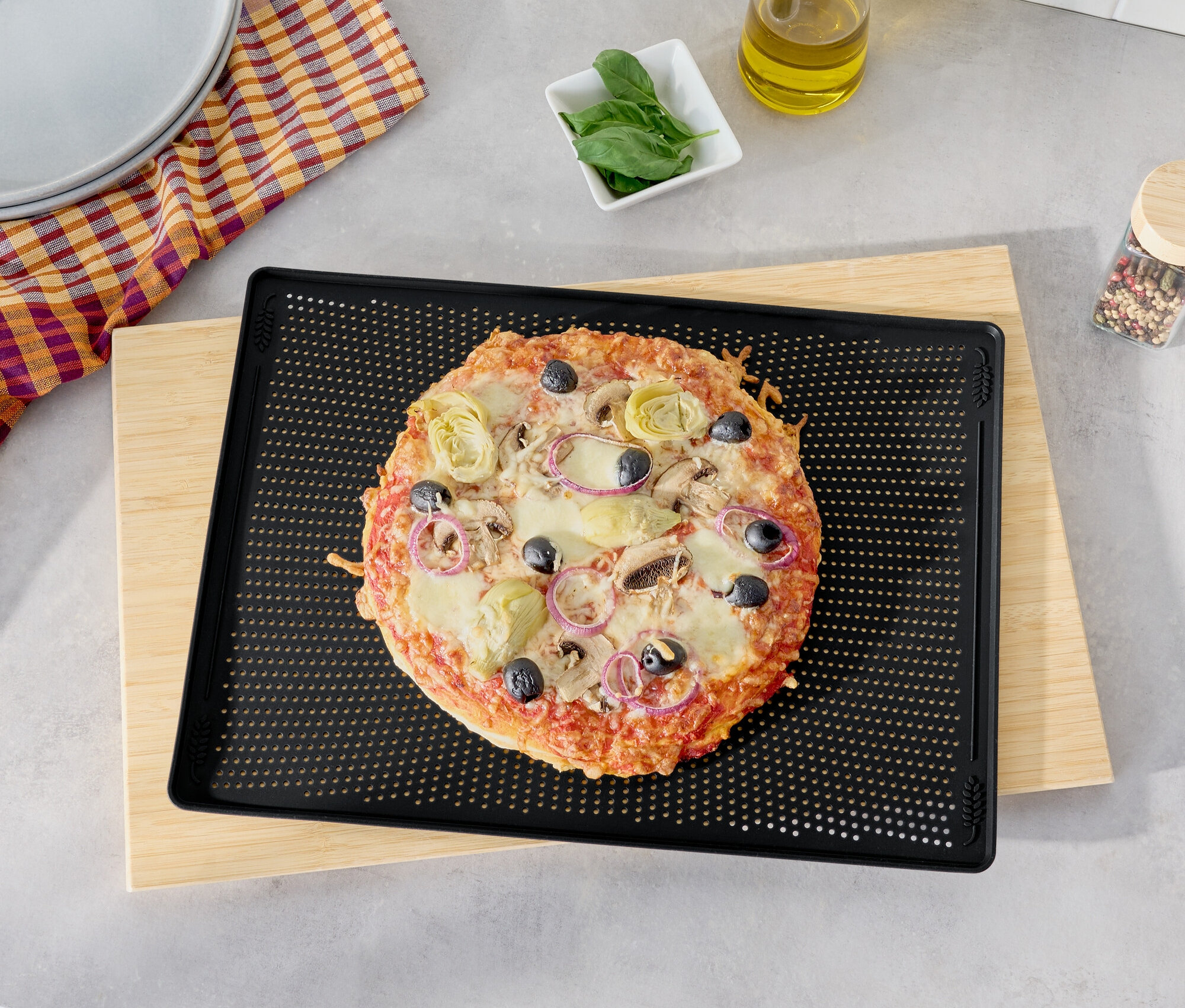 Pizza mit Oliven, Artischocken und roten Zwiebeln auf einem schwarzen Backblech auf einem Holzbrett.