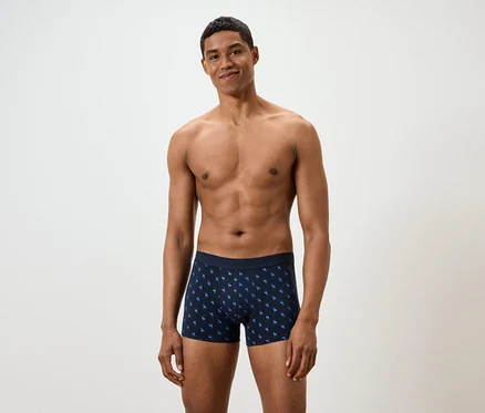 Mann posiert vor weißem Hintergrund in blauen Boxershorts mit Muster.