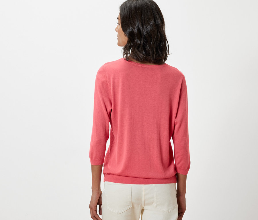 Frau trägt einen korallenroten Feinstrickpullover mit Seide und eine weiße Hose.