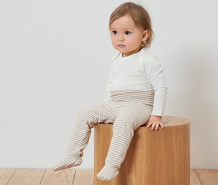 Ein Kind sitzt auf einem Holzhocker und trägt 3 Baby-Strampelhosen.