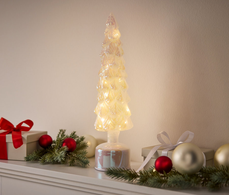 Ein dekorativer, beleuchteter Baum steht zwischen Geschenken und Ornamenten.