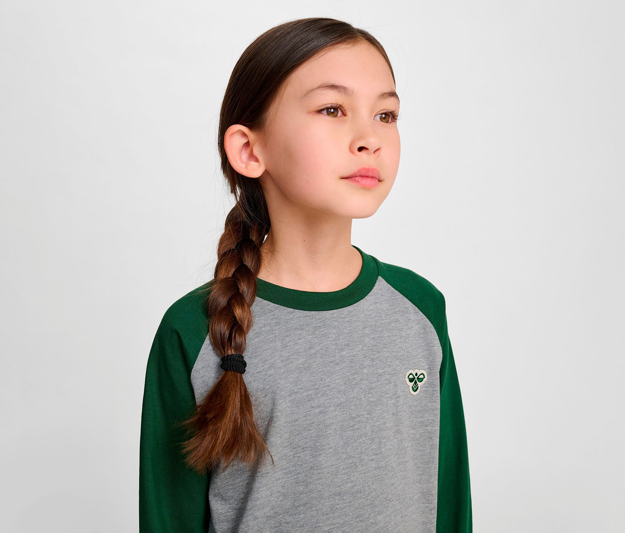 Mädchen mit Zopf trägt ein grünes HUMMEL HMLJR Raglan Loose T-Shirt.