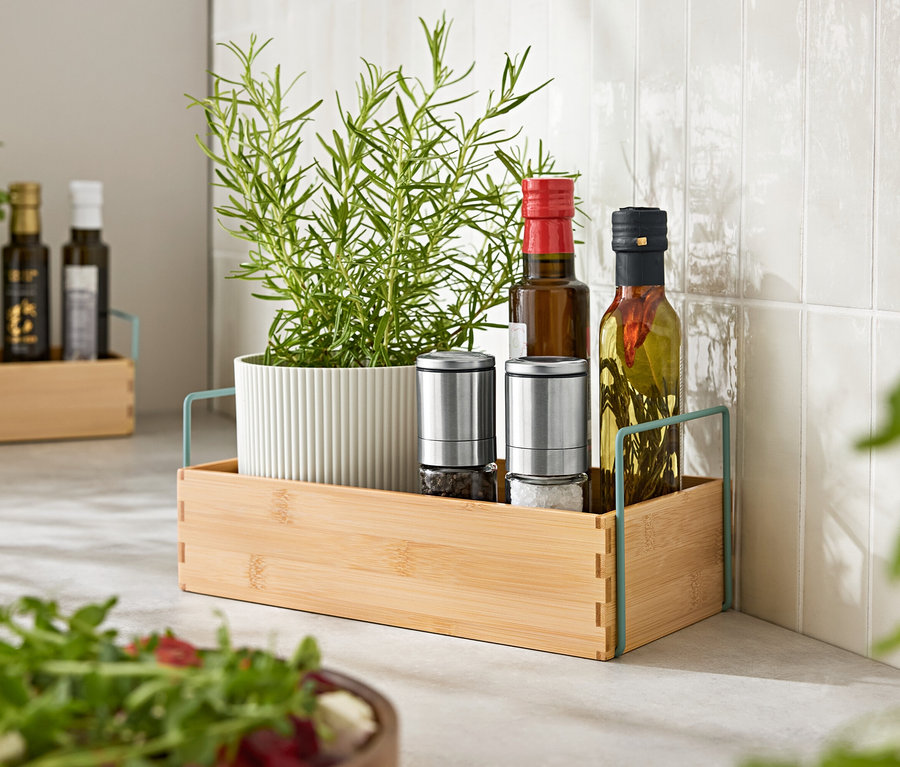 Kräuter im Topf, zwei Gewürzmühlen und zwei Ölflaschen in einem Holztablett.