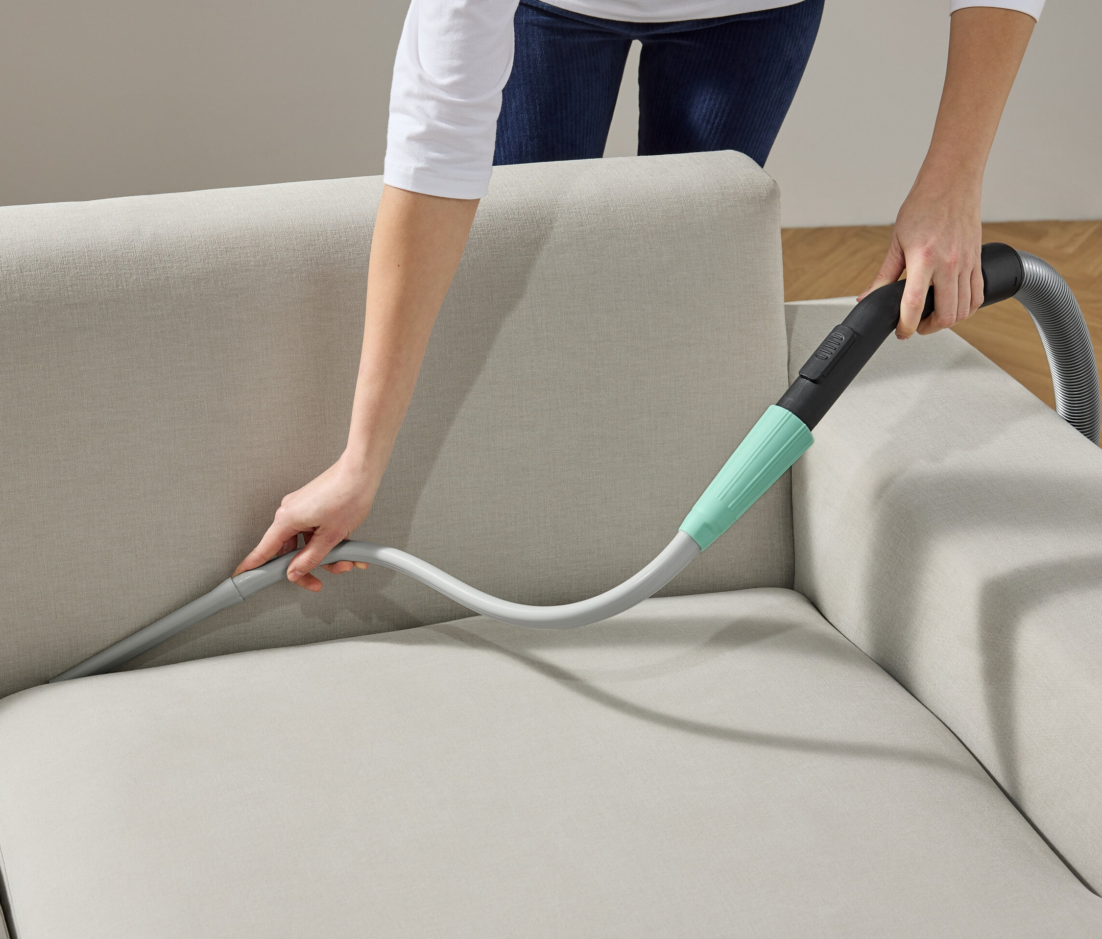 Frau reinigt Sofa mit Staubsauger-Aufsatz.