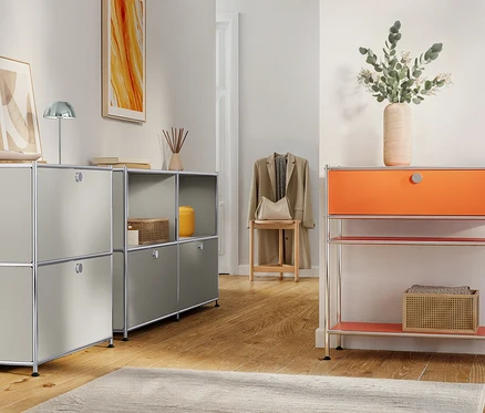 Einrichtungsszene mit grauen und orangefarbenen modularen Aufbewahrungseinheiten, dekorativen Gegenständen und einer Jacke auf einem Hocker.