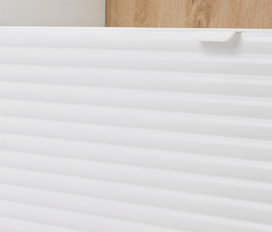 Detailansicht eines weißen Schranks mit horizontalen Rillen und einem hellbraunen Holzelement im Hintergrund.