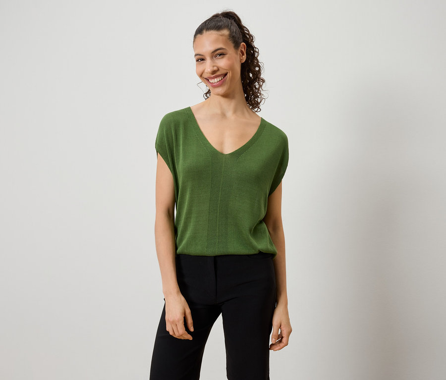Frau trägt ein grünes Top und eine schwarze Hose.