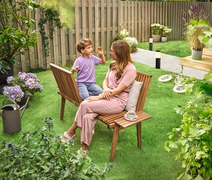 Eine Frau sitzt mit einem Kind auf einer flexiblen Plauderbank im Garten. Im Hintergrund sind zwei geriffelte Solar-Wegeleuchten zu sehen.