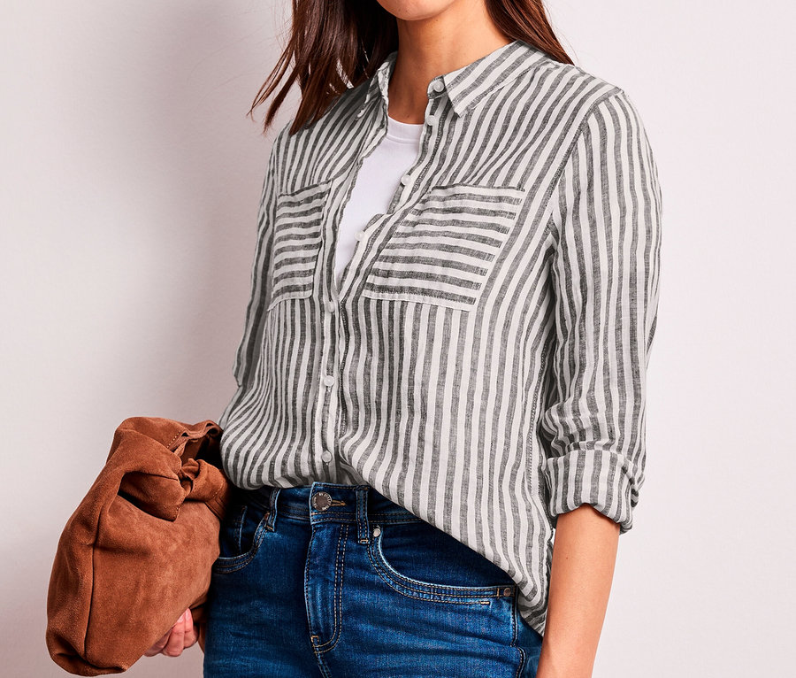 Frau trägt eine dunkelbraun-weiß gestreifte Street One Hemdbluse über einem weißen T-Shirt, blaue Jeans und hält eine braune Clutch.