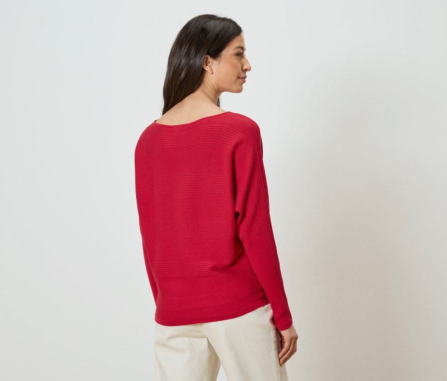 Frau von hinten in rotem Pullover und beigen Hosen.