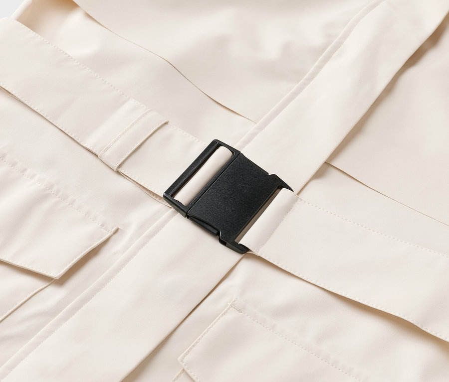 Nahaufnahme eines beigen Kleidungsstücks mit Taschen und einem schwarzen Schnallenverschluss.