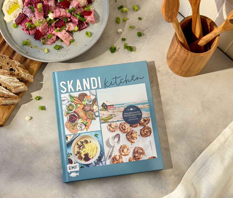 Aufnahme eines Kochbuchs mit dem Titel 'Skandi Kitchen' neben einem Teller mit Rote-Bete-Salat, Brot und Kochutensilien.