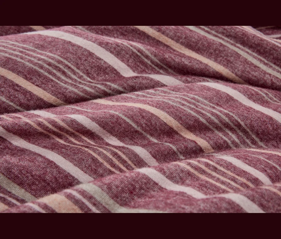Nahaufnahme eines weichen, gefalteten Stoffes mit Streifen in Rot-Violett, Cremeweiß und hellem Pfirsich.