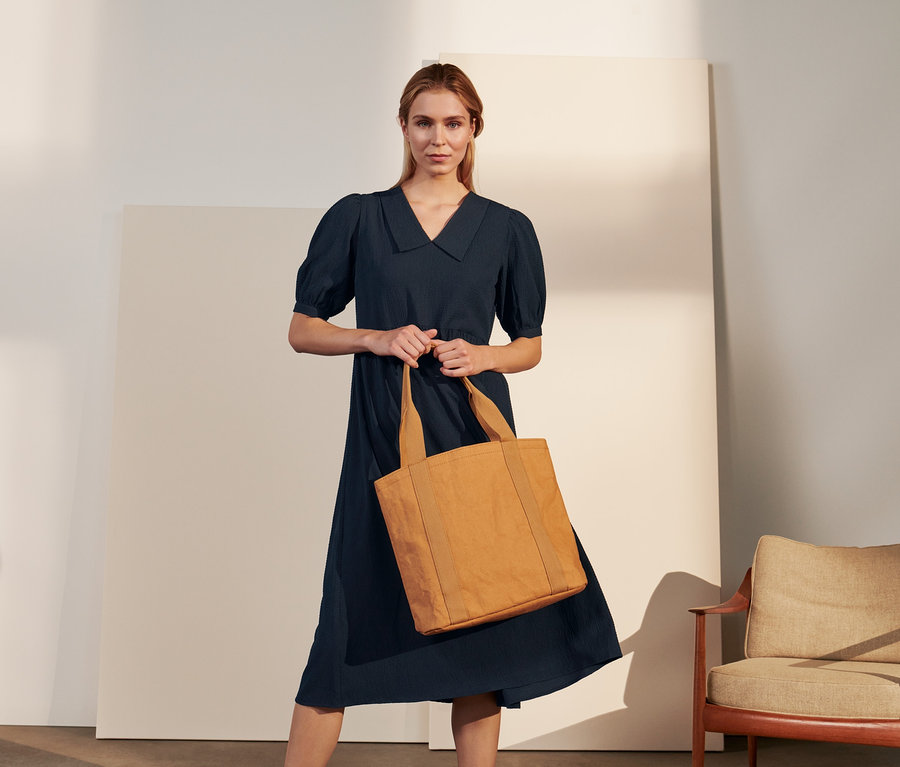 Frau hält eine Tragetasche und trägt ein gekrepptes Blusenkleid.