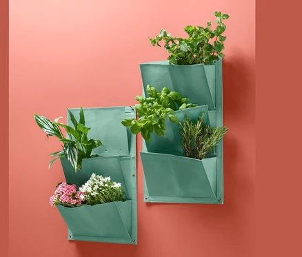 Zwei grüne Pflanztaschen »Vertikalbeet« mit Pflanzen an einer korallfarbenen Wand.