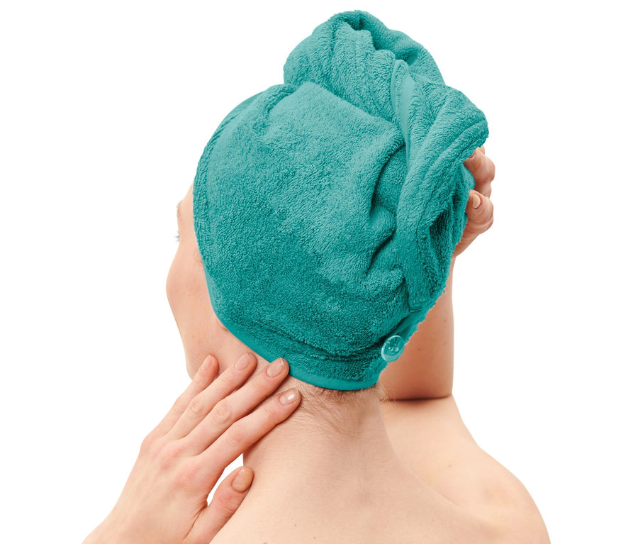 Frau trägt ein Turban-Handtuch in Aqua und berührt ihren Nacken.