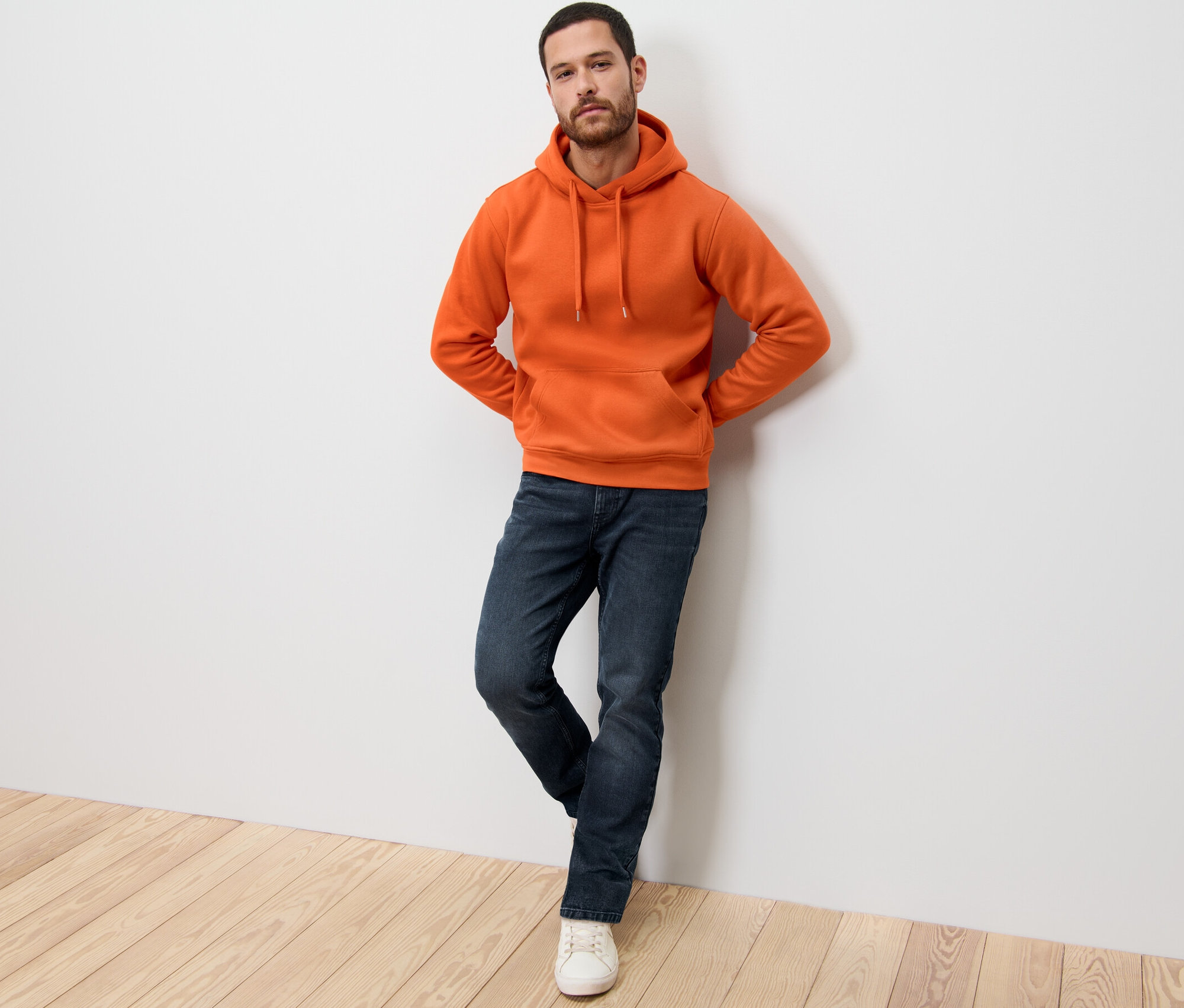 Mann lehnt an Wand, trägt orangefarbenen Hoodie.