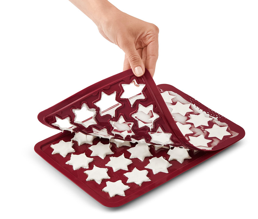 Eine Hand hebt eine rote Zimtstern Backmatte mit weißen Sternen an.