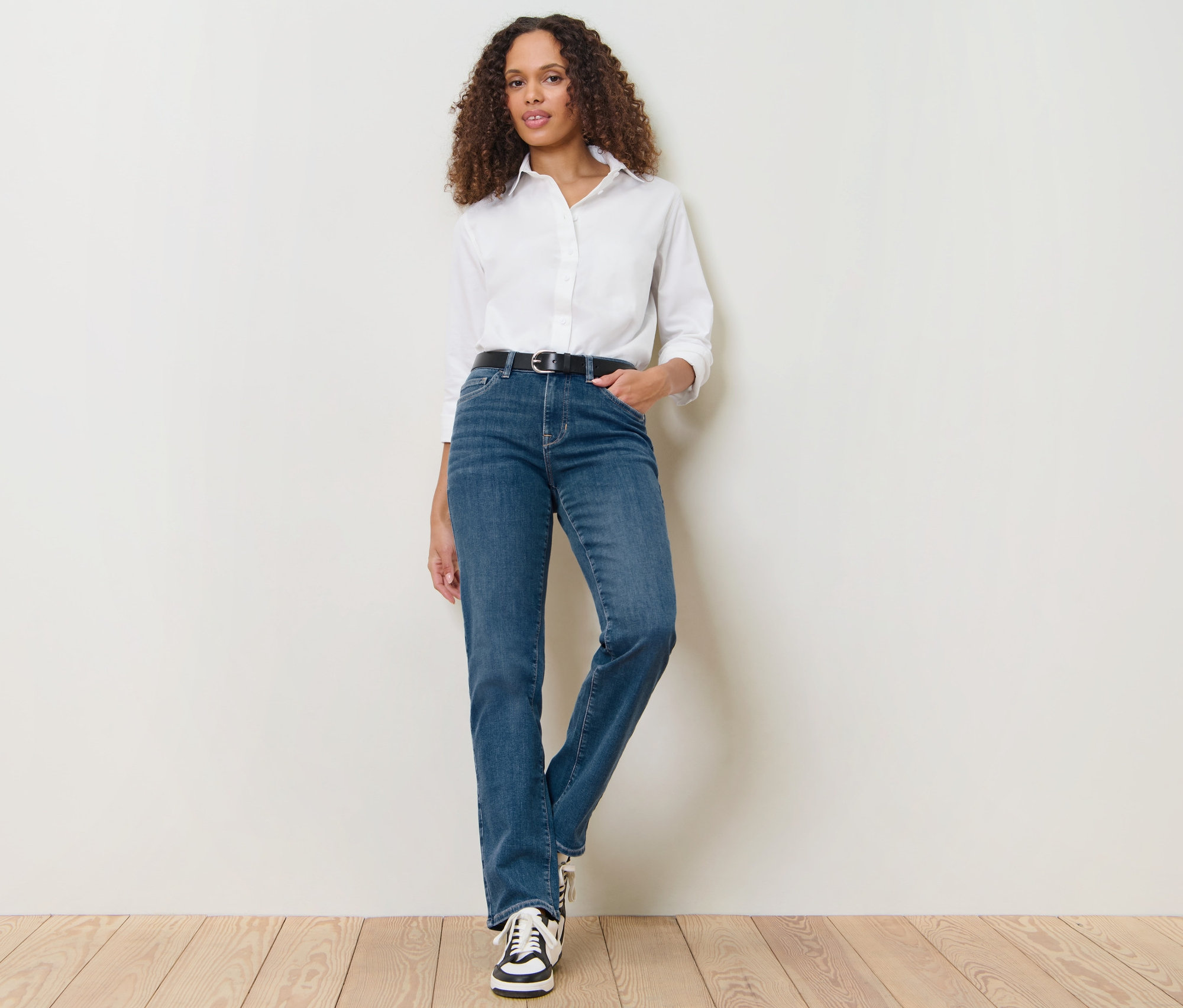 Frau posiert in Straight Jeans – Fit »Kira«, mittelblau, weißem Hemd und Turnschuhen.