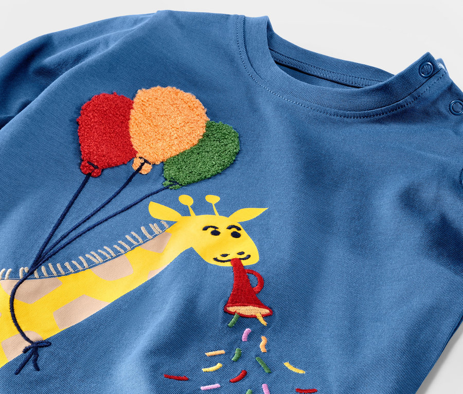 Blaues Langarmshirt mit Giraffe, die eine Geburtstagströte und Ballons hält.