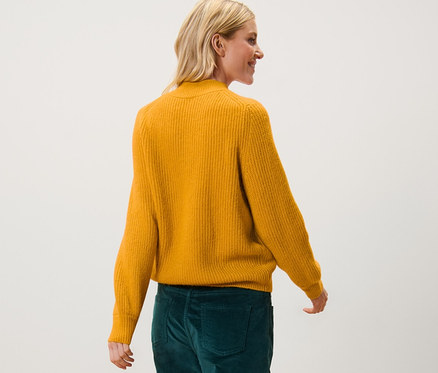 Frau geht in Grobstrickpullover und grüner Hose.