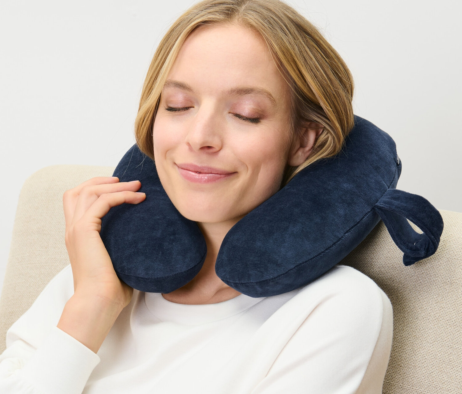 Frau sitzt mit blauem Nackenkissen, Memory Foam, im Sessel.