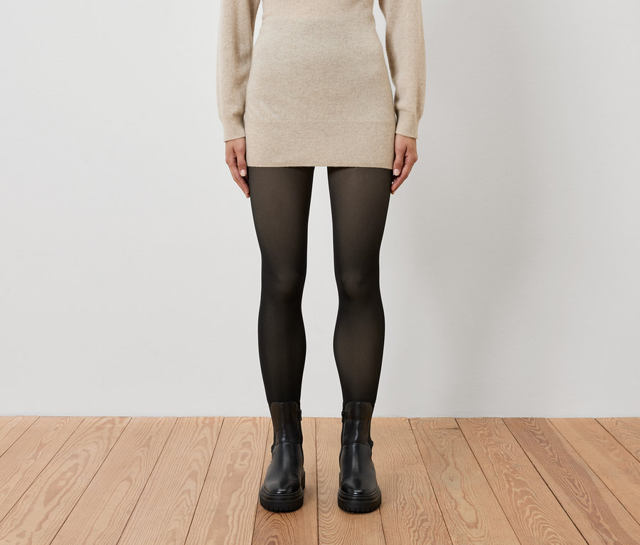 Frau trägt ein beiges Kleid, schwarze Strumpfhose und schwarze Stiefel.