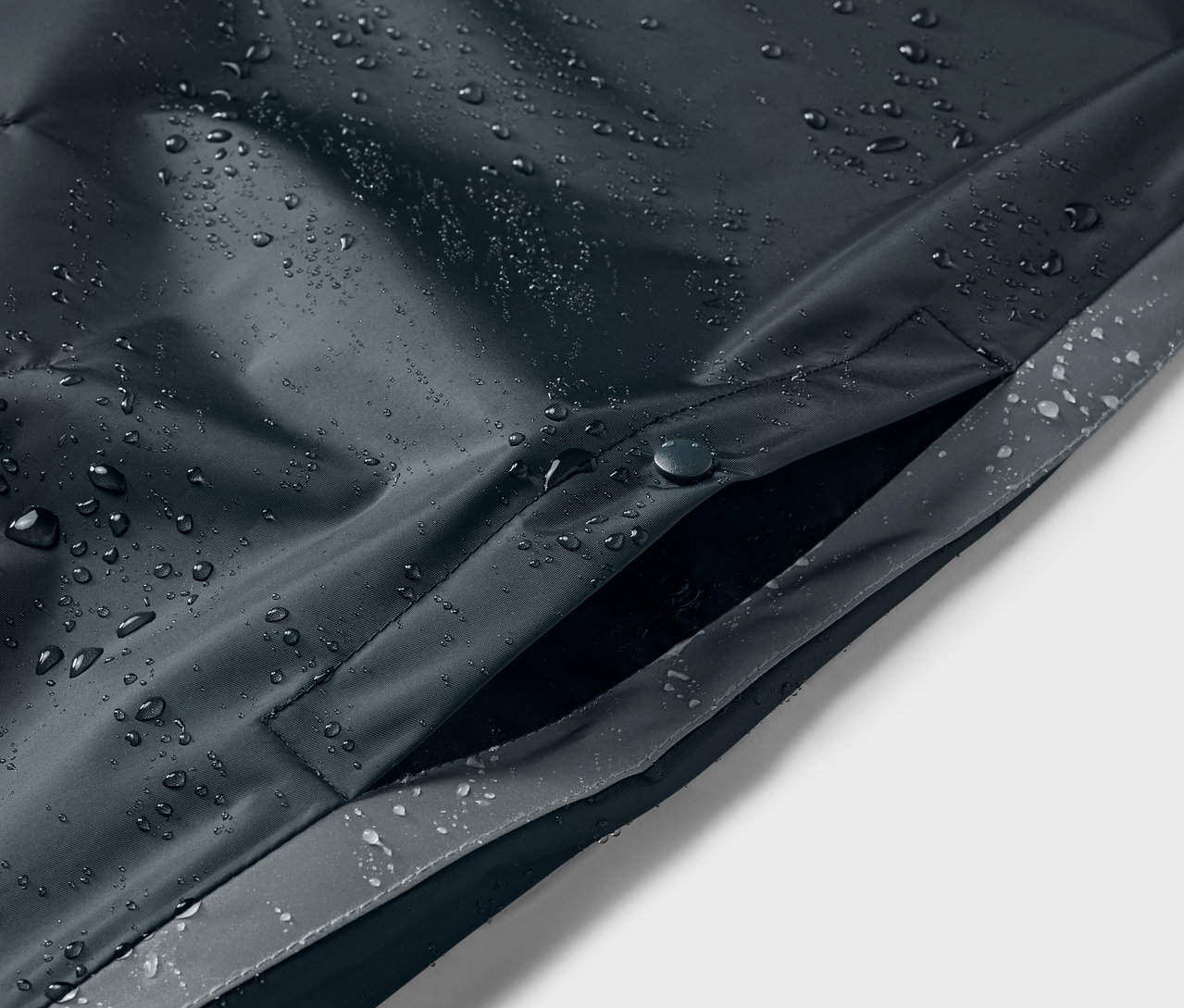 Detailansicht eines blauen Kinder-Regenponchos mit Wassertropfen und Tasche.