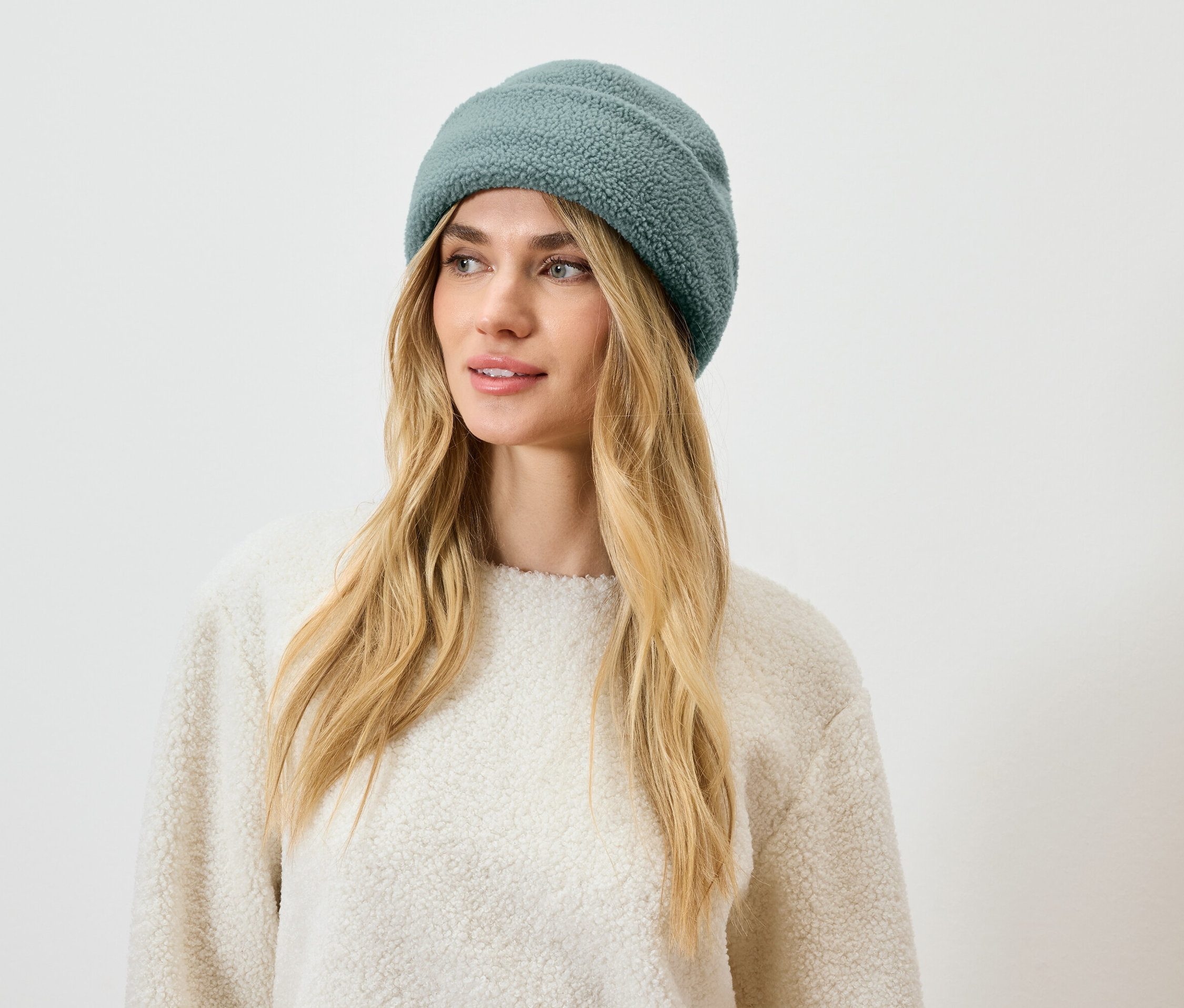 Frau mit blonden Haaren und einer blaugrünen Mütze.