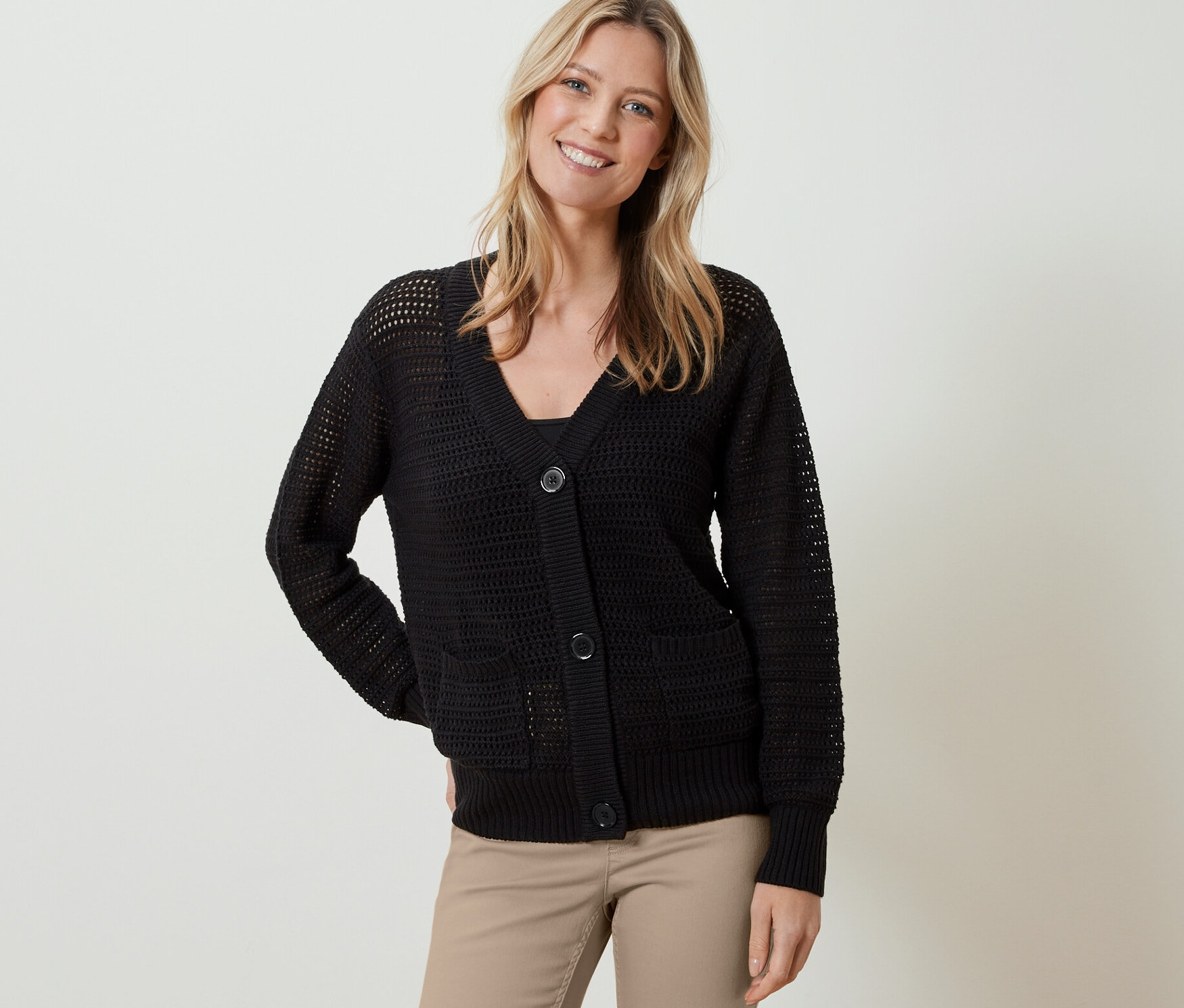 Frau trägt einen schwarzen Cardigan in Pointellestrick und eine beige Hose.