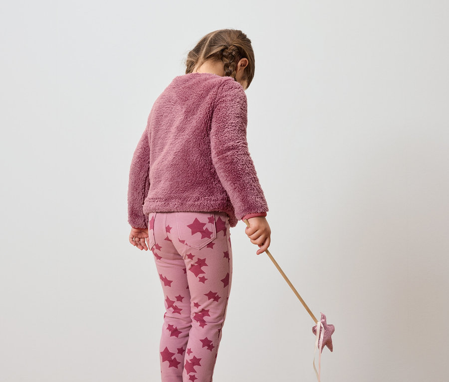 Mädchen in rosa Pullover und Hose mit Sternenmuster hält einen Stab mit einem Stern.