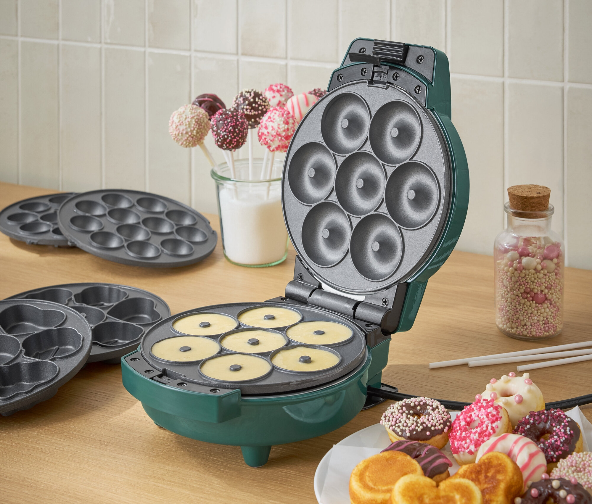 Grüner Donut-Maker mit Teig und einem Teller fertiger Donuts.