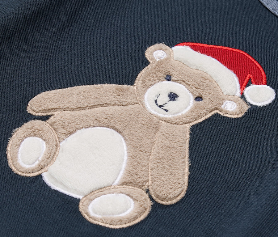 Auf einem dunkelblauen Stoff befindet sich ein brauner Teddybär mit einer roten Weihnachtsmütze.