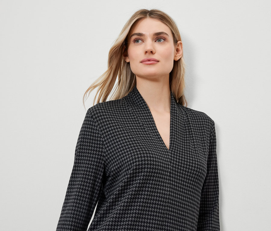 Blonde Frau trägt ein Kleid mit Hahnentrittmuster und V-Ausschnitt.