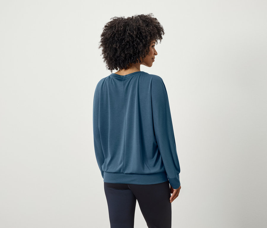 Rückansicht einer Frau mit Afro-Frisur in einem blauen Langarmshirt und dunkelblauen Hosen.