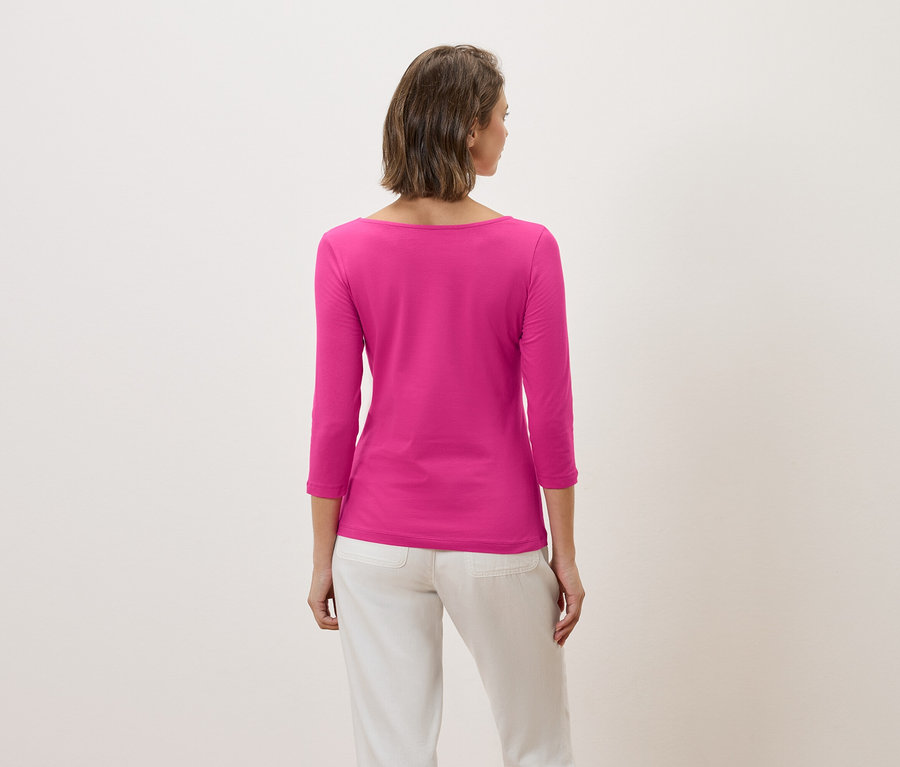 Rückansicht einer Frau mit kurzen braunen Haaren, die ein pinkfarbenes Dreiviertelarm-Shirt und weiße Hosen trägt.