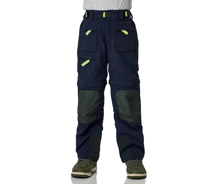 Junge trägt eine marineblaue Jako-O Zipp-off-Hose und grüne Schuhe.