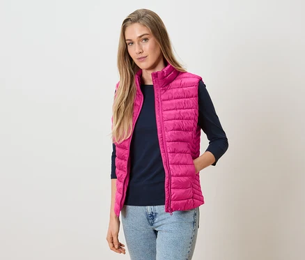 Frau trägt eine pinke Steppweste über einem marineblauen Langarmshirt und Jeans.