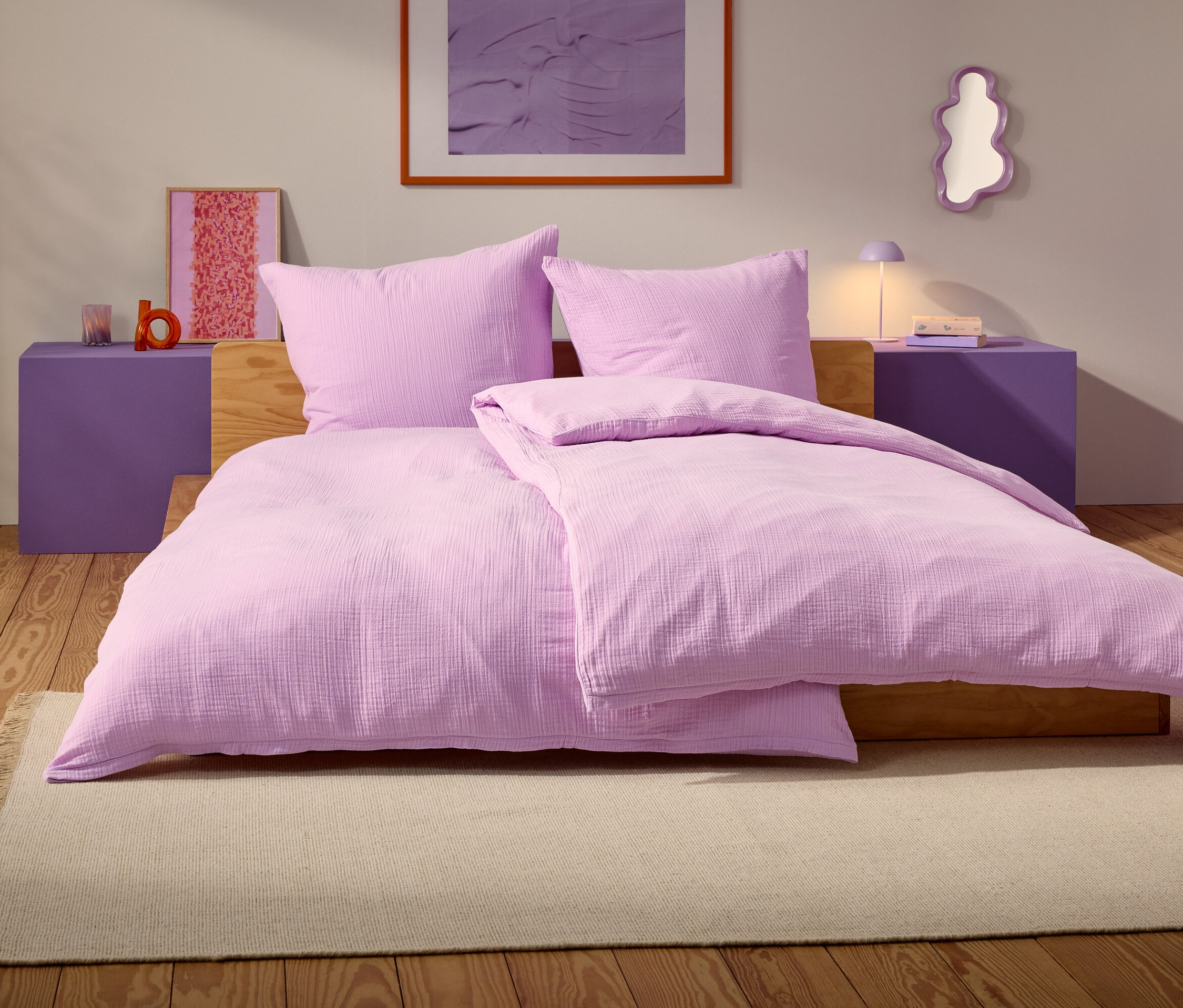 Ein lila Bett mit zwei Kissen und einer Decke steht auf einem beige Teppich in einem Schlafzimmer.